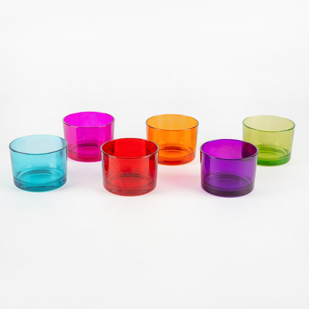 Bicchieri di vetro colorati in varie tonalità: blu, rosa, rosso, arancione, viola e verde, su sfondo bianco.