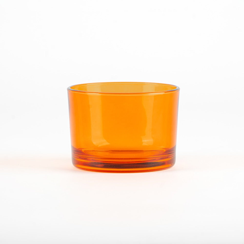 Bicchiere di vetro trasparente arancione con base spessa, posizionato su sfondo bianco.