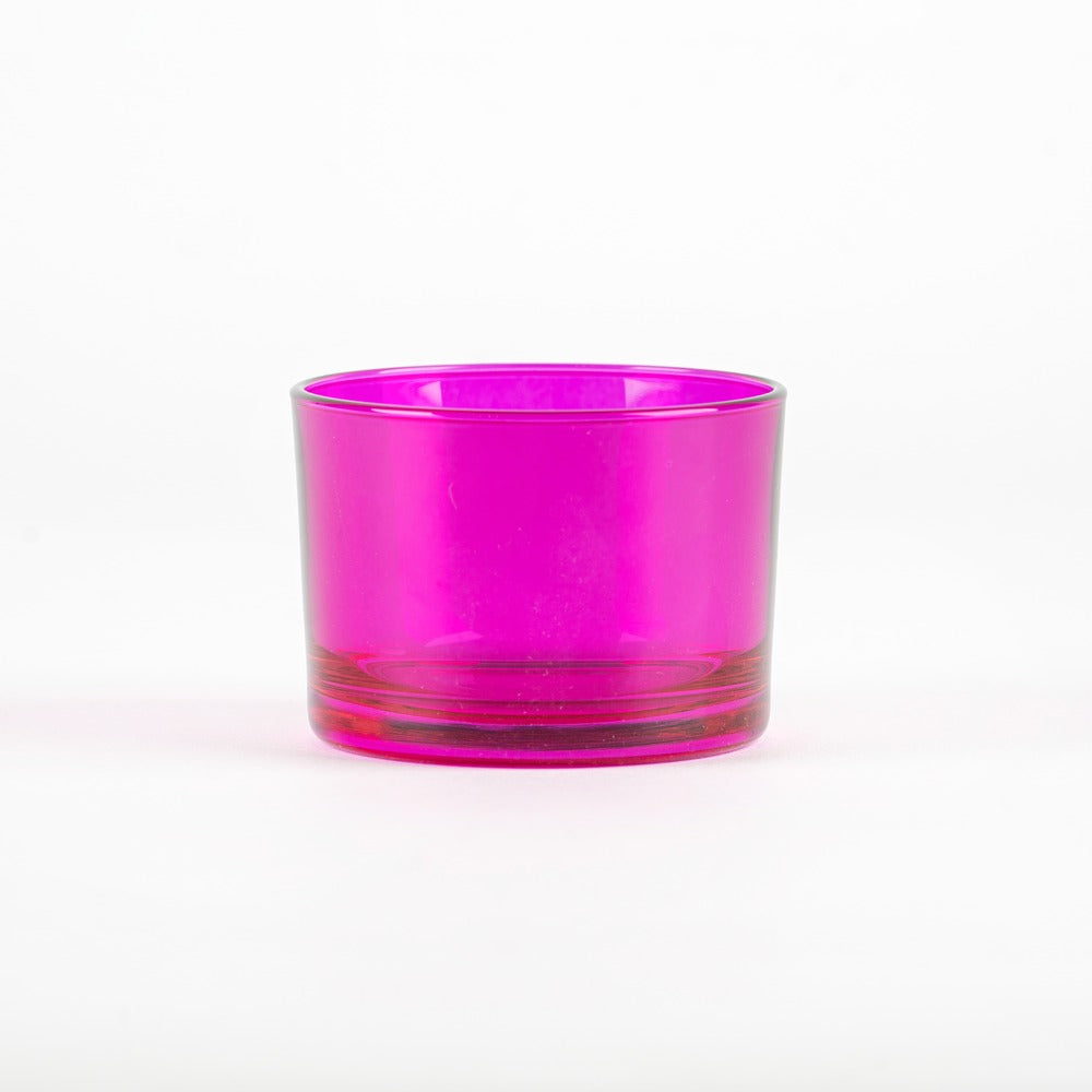 Bicchiere di vetro trasparente di colore fucsia, con base liscia e forma cilindrica, su sfondo bianco.