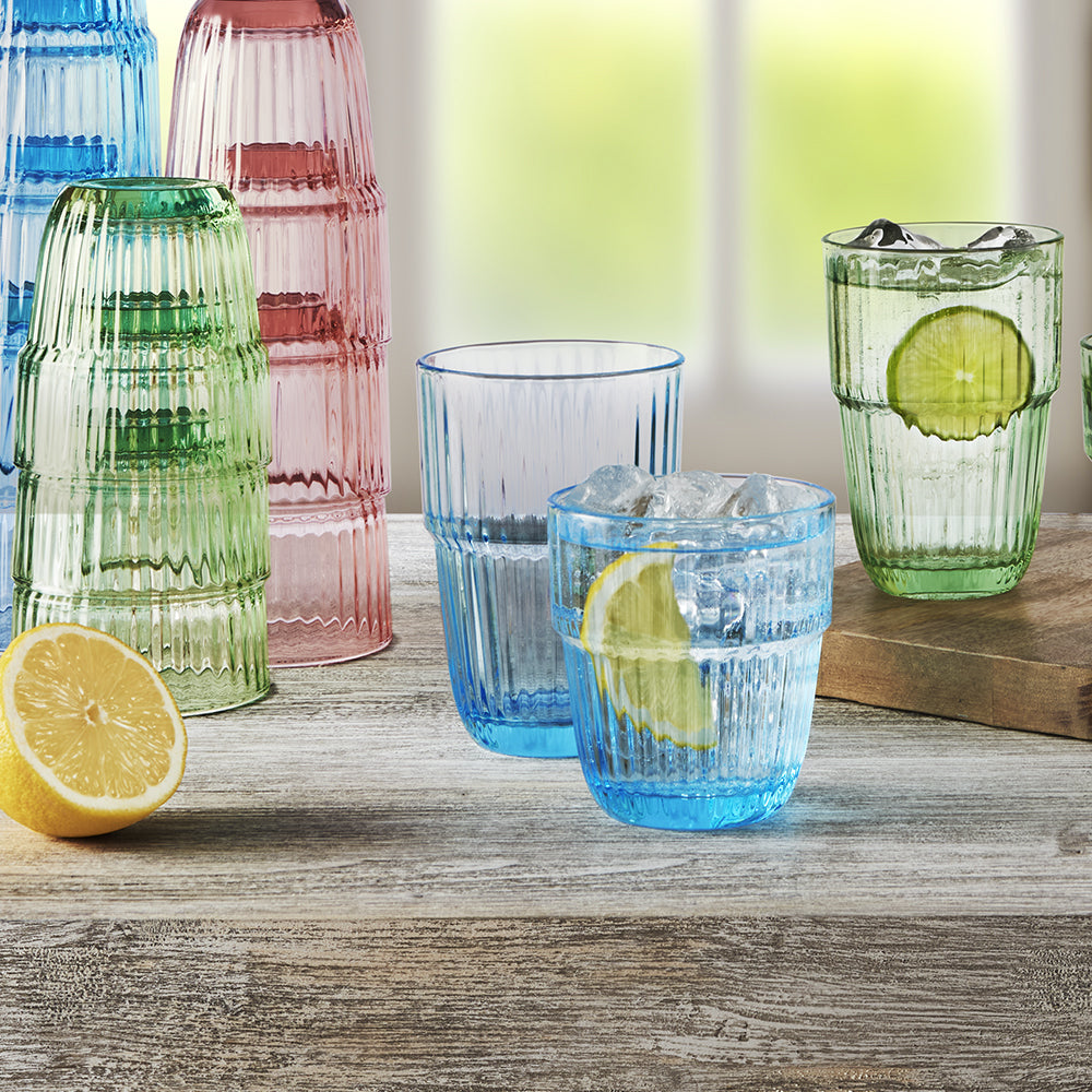 Bicchieri di vetro colorati blu, verde e rosa con motivo a righe su tavolo di legno con limone e ghiaccio