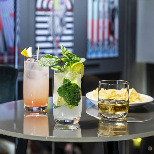 tre bicchieri, uno con cocktail rosa e fettina di limone, uno con mojito con lime e menta, uno con liquore ambrato, tavolo con piatto di