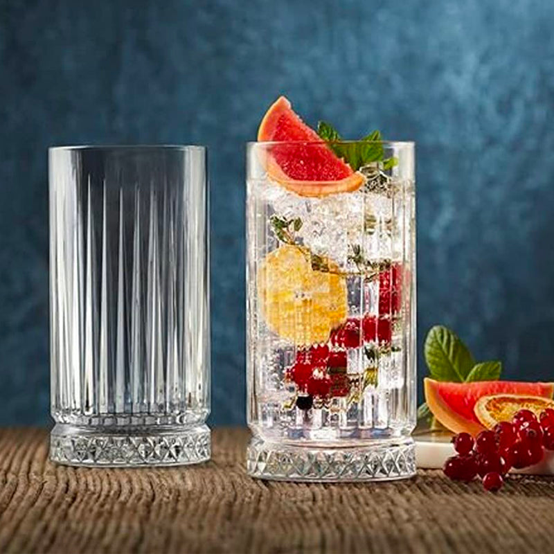 Due bicchieri di vetro trasparente con decorazioni e scanalature, uno vuoto e uno con acqua, ghiaccio, frutta e foglie verdi, su superficie