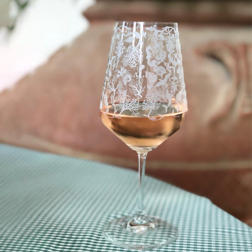 Glas mit floralen und maritimen Gravuren, mit Roséwein gefüllt, auf grün-weiß kariertem Tischtuch.
