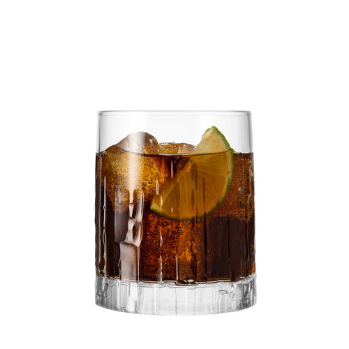 Cocktail scuro in un bicchiere trasparente con ghiaccio e una fetta di lime. Fondo annerito e texture rigata.