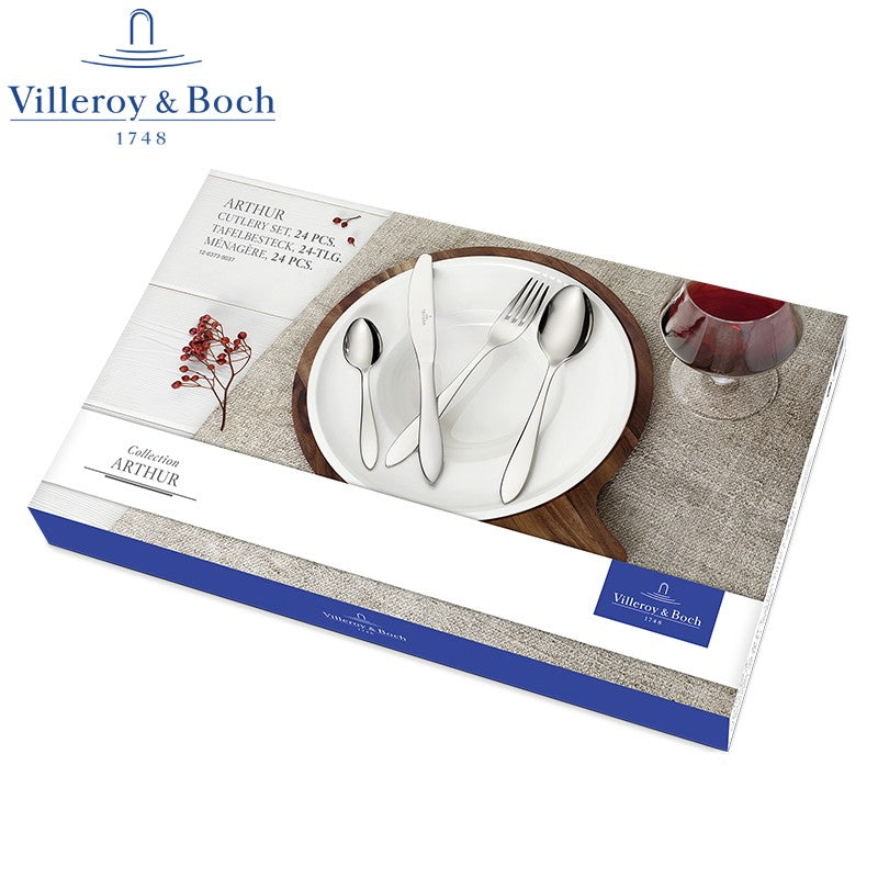 Set di posate in acciaio inox lucido, coltello, forchetta e due cucchiai disposti su piatto bianco con bordo legno, bicchiere con vino