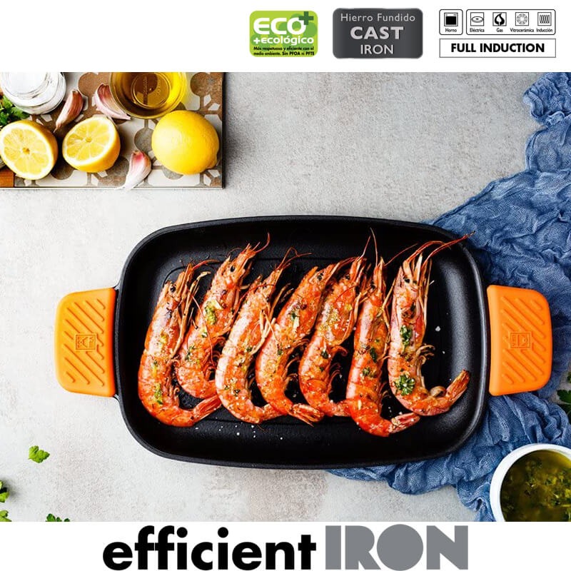 Crevettes grillées sur une poêle noire à poignées orange, accompagnées de citrons et herbes aromatiques dans un cadre lumineux.