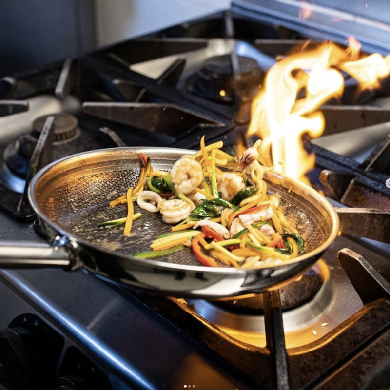 Stahlpfanne mit Garnelen, sautiertem Gemüse und Flamme auf Gasherd.