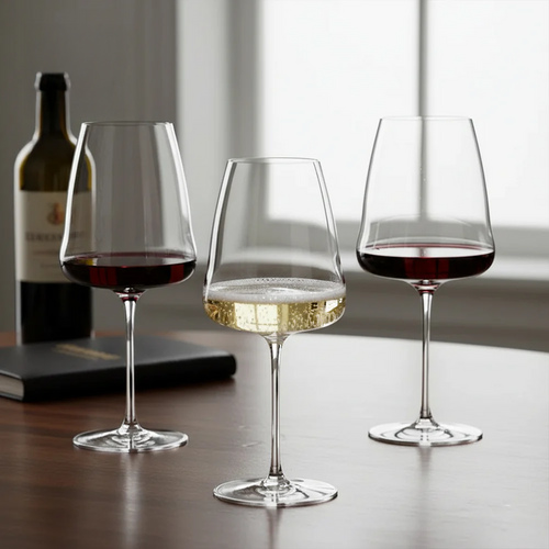 Trois verres à vin en verre transparent avec vin rouge et blanc sur table en bois, derrière bouteille de vin et livre noir.