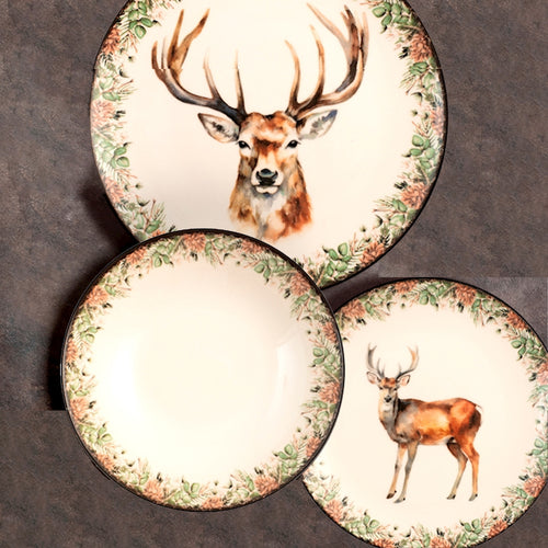 Set di tre piatti in ceramica bianca decorati con motivi di cervi e bordi con foglie verdi e pigne marroni su sfondo scuro.