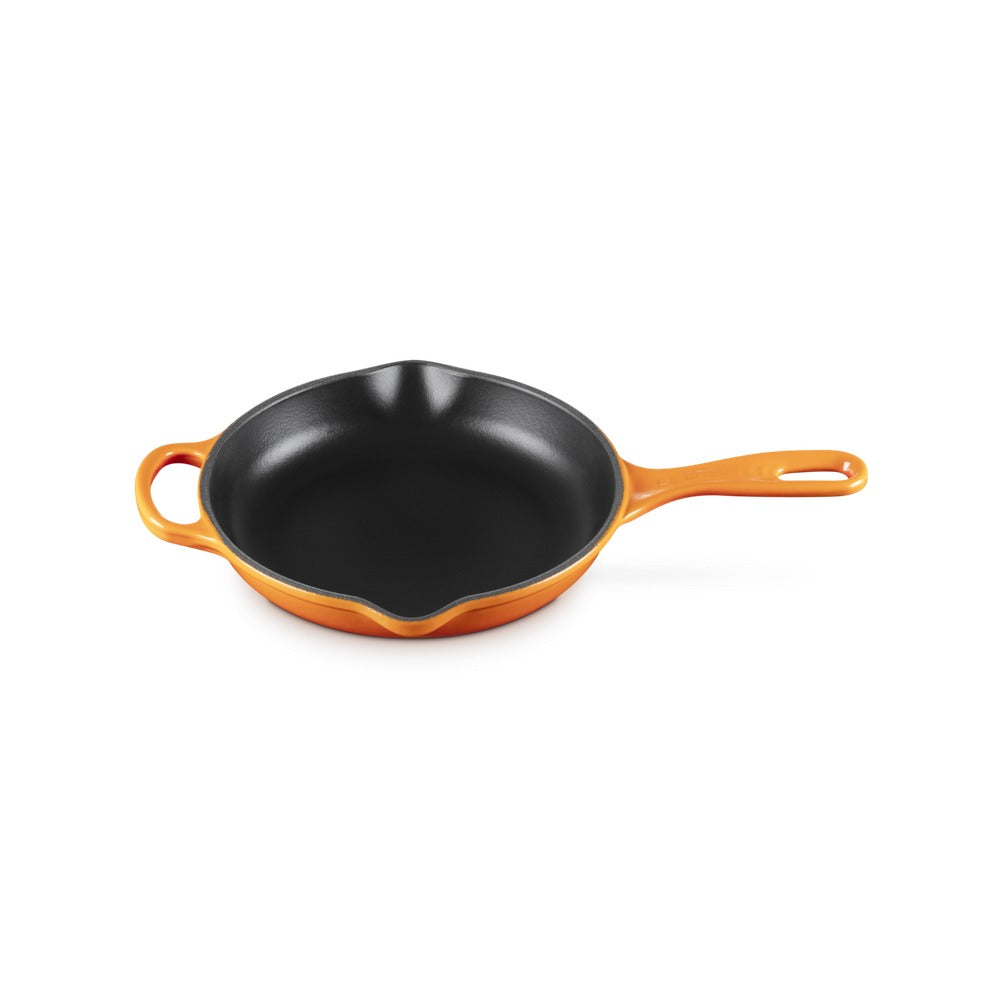 Cocotte en fonte orange avec long manche et fond noir brillant, en position verticale sur fond blanc.