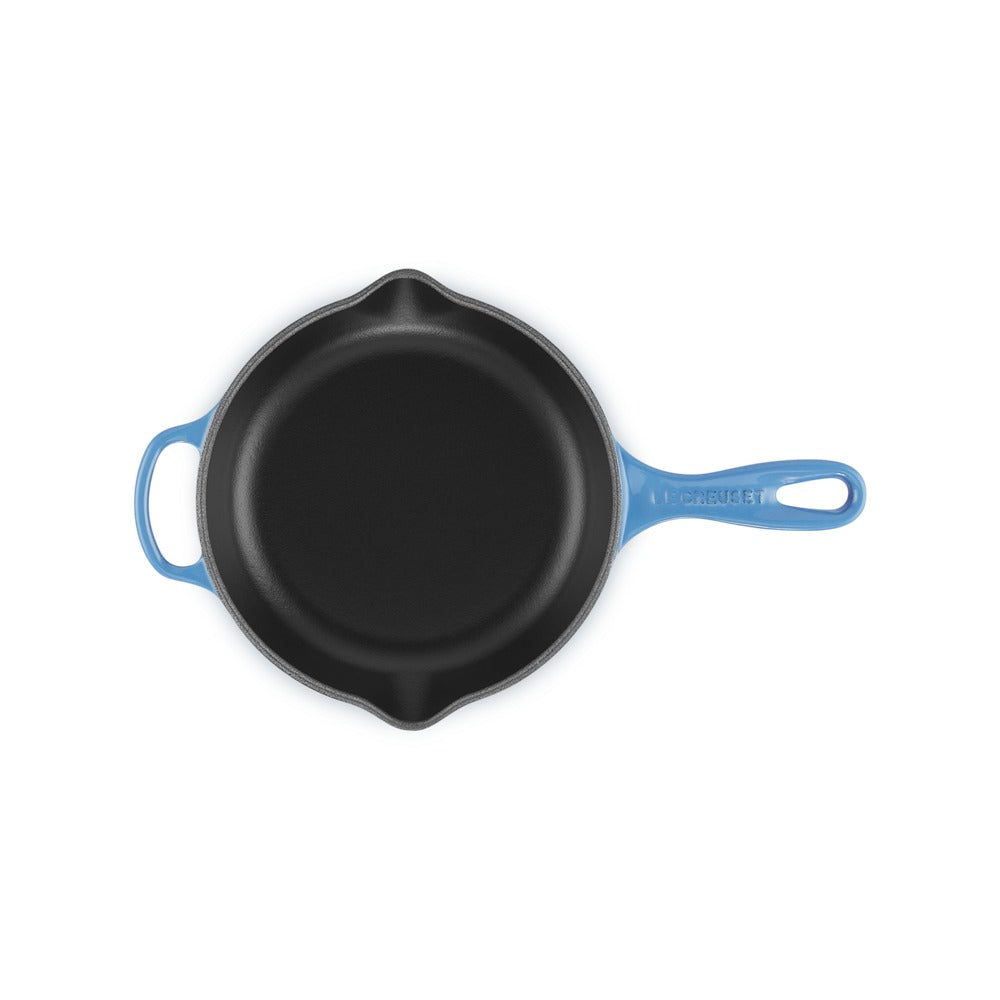 Poêle en fonte avec manche bleu, surface intérieure noire et lisse, forme ronde, sur fond blanc.
