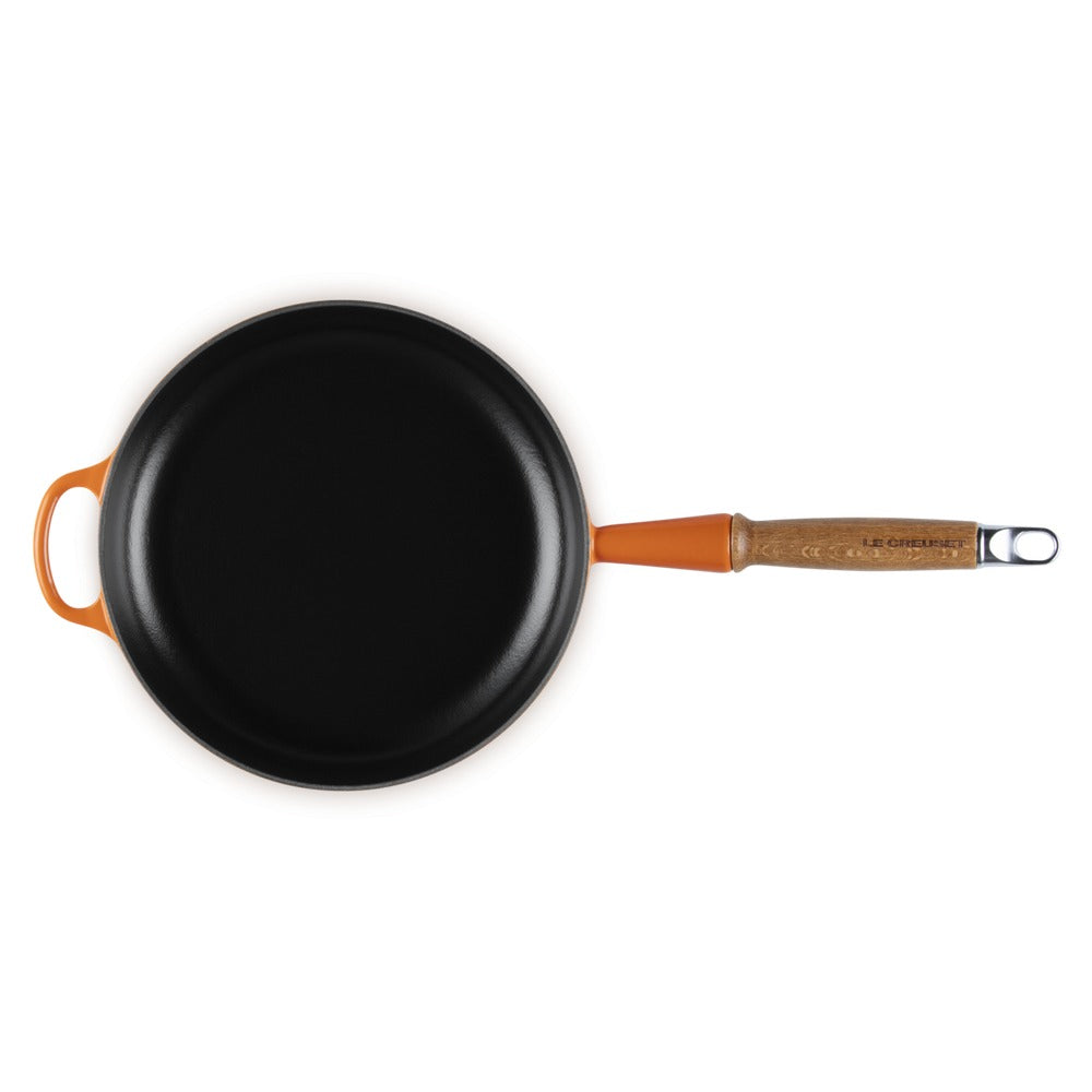 Poêle ronde avec revêtement noir et manche orange en matériau apparemment bois. Fond blanc.