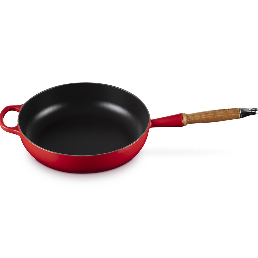 Padella rotonda di colore rosso con manico in legno e superficie interna nera. Sfondo bianco.