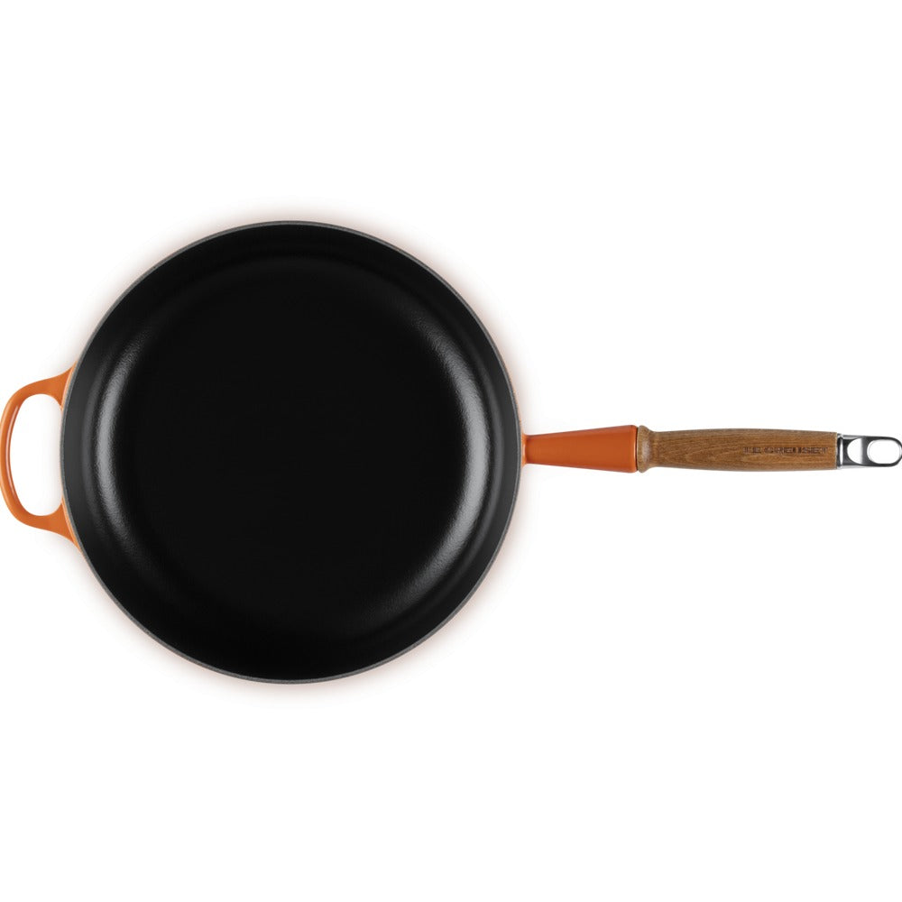 Padella nera con manico arancione e legno, superficie brillante, vista dall'alto.