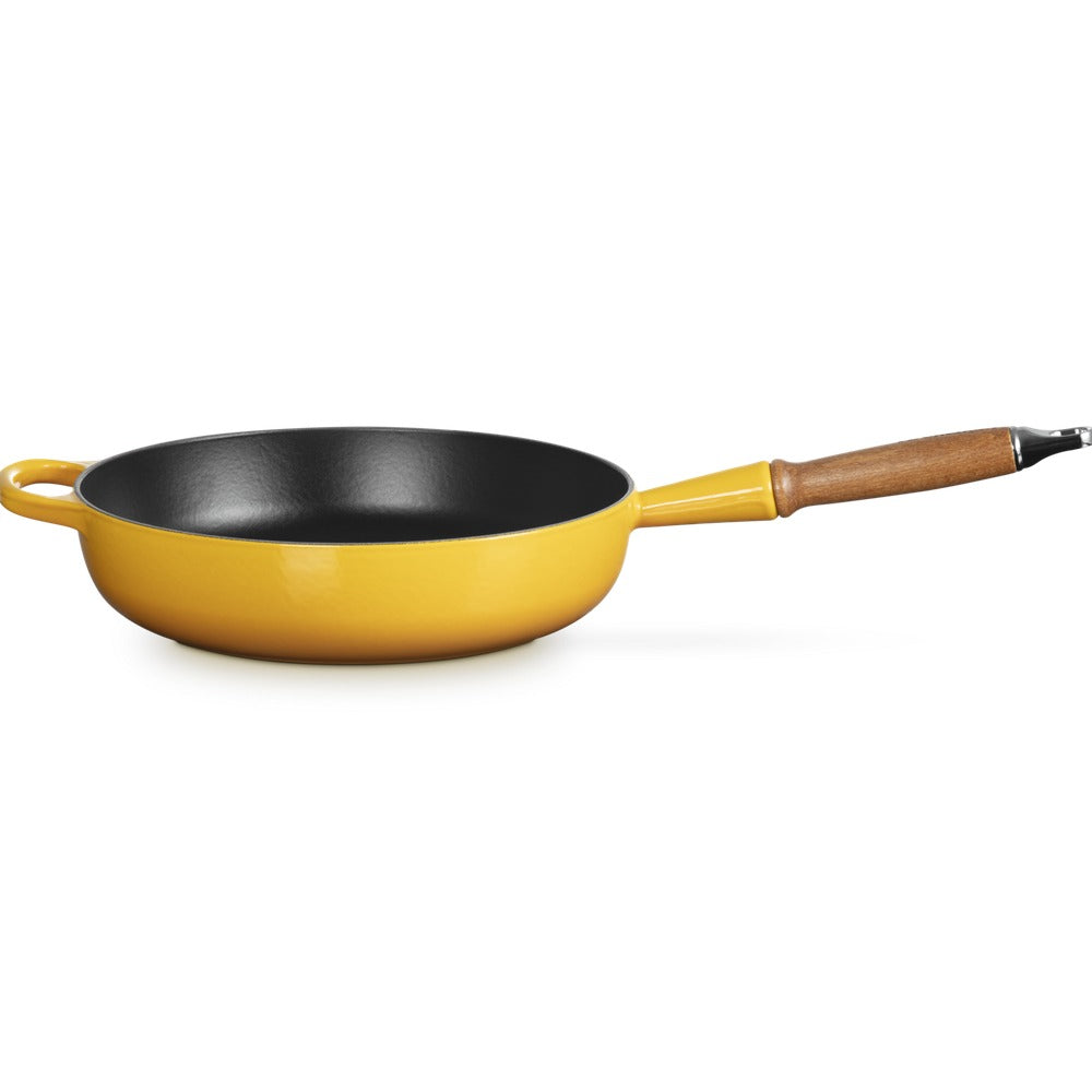 Padella gialla con manico in legno, superficie interna nera e fondo lucido, leggermente inclinata su sfondo bianco.
