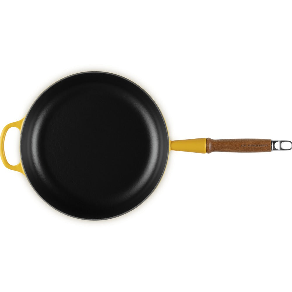 Padella rotonda nera con manico in legno e dettagli gialli, senza ingredienti visibili, su sfondo bianco.