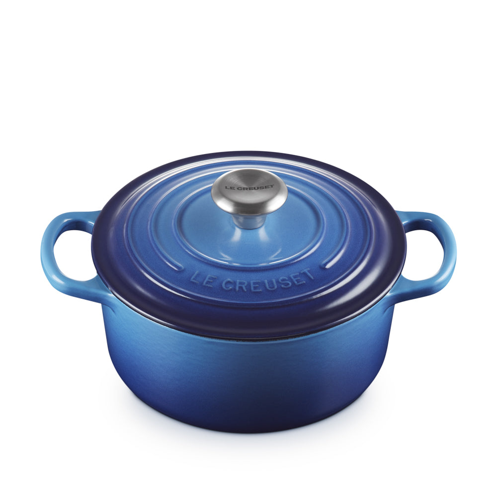Cocotte rotonda smaltata in ceramica blu sfumato con manici laterali, coperchio con pomolo metallico e logo LE CREUSET in rilievo.