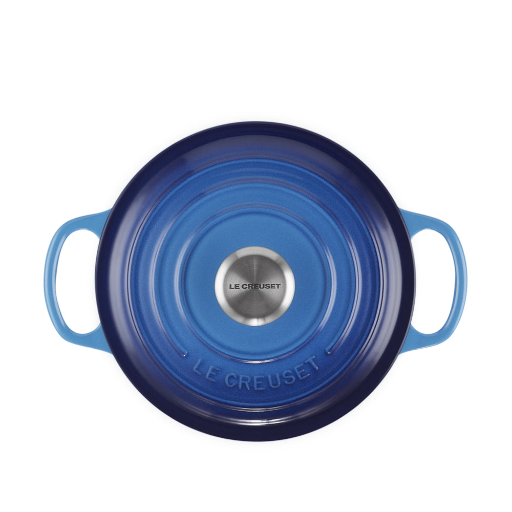 coperchio rotondo in metallo smaltato blu con manici laterali e pomello centrale in acciaio con scritta Le Creuset, su sfondo bianco