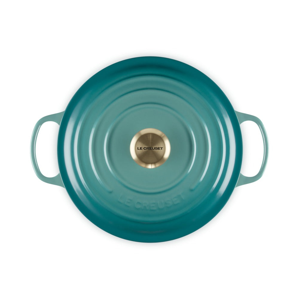 Casseruola ovale di colore turchese con manici, superficie liscia e centrale dorato con scritta "LE CREUSET".