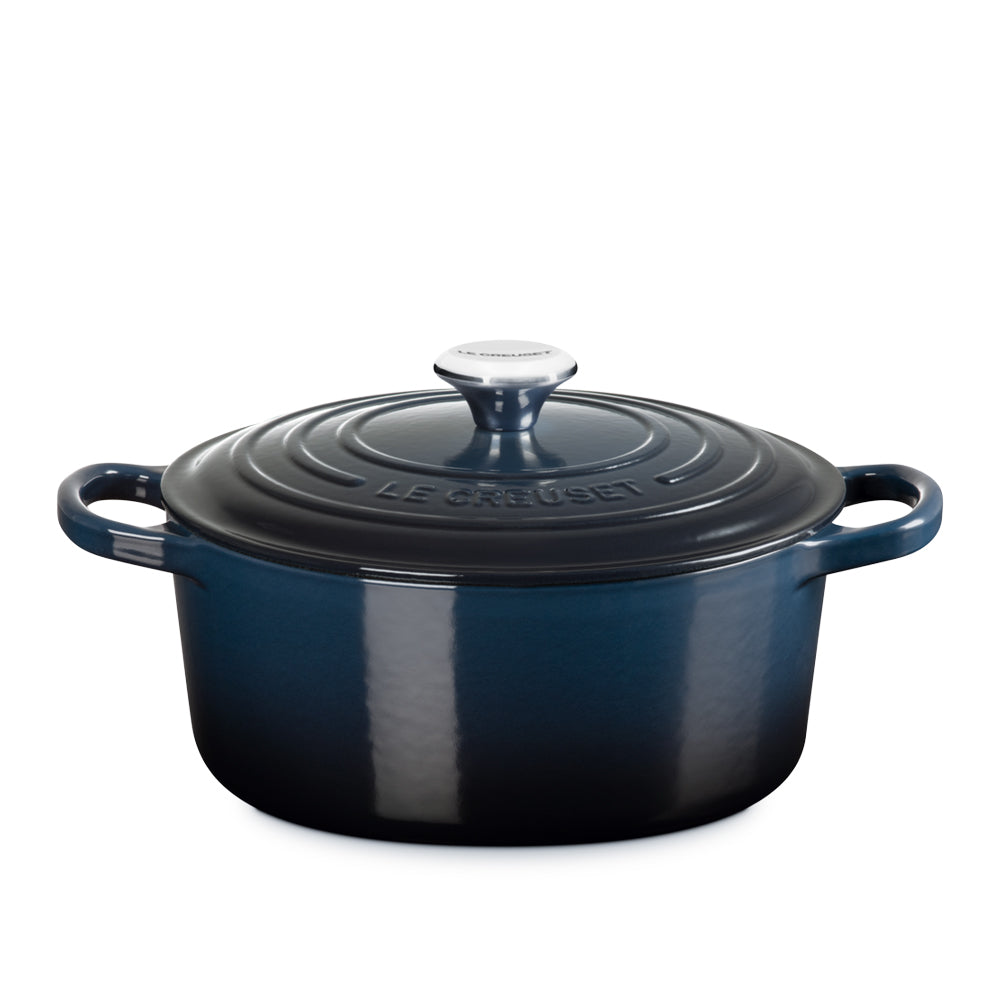 pentola ovale in ghisa smaltata blu scuro con coperchio della stessa tonalità e manici laterali, con manopola bianca e scritta Le Creuset sulla parte