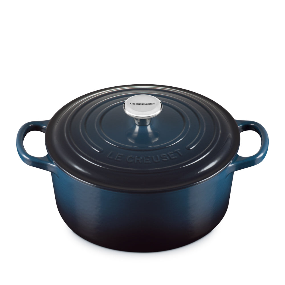 Pentola ovale in ghisa smaltata blu scuro con coperchio e manici laterali, pomello in acciaio con scritta Le Creuset, sfondo bianco