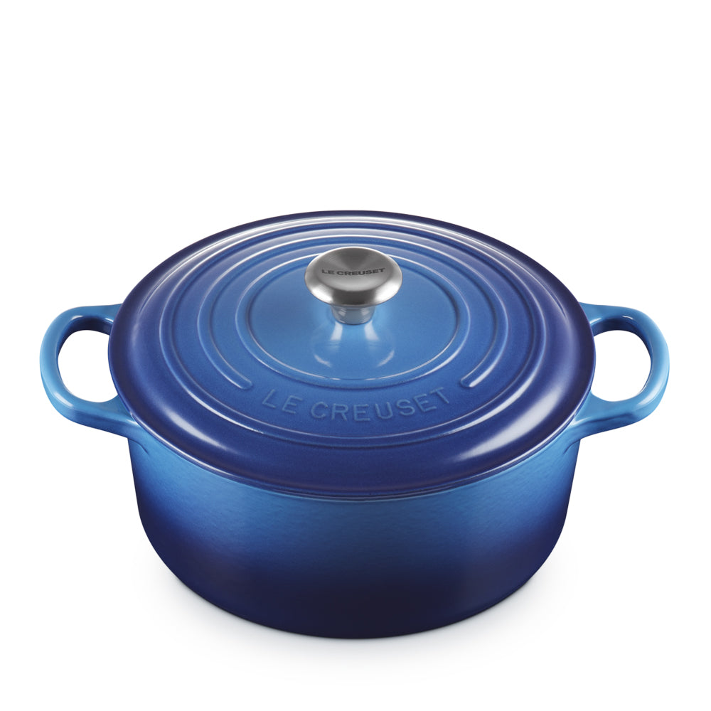pentola in ghisa smaltata blu con coperchio tondo e manici laterali, pomello in metallo con logo LE CREUSET, sfondo bianco