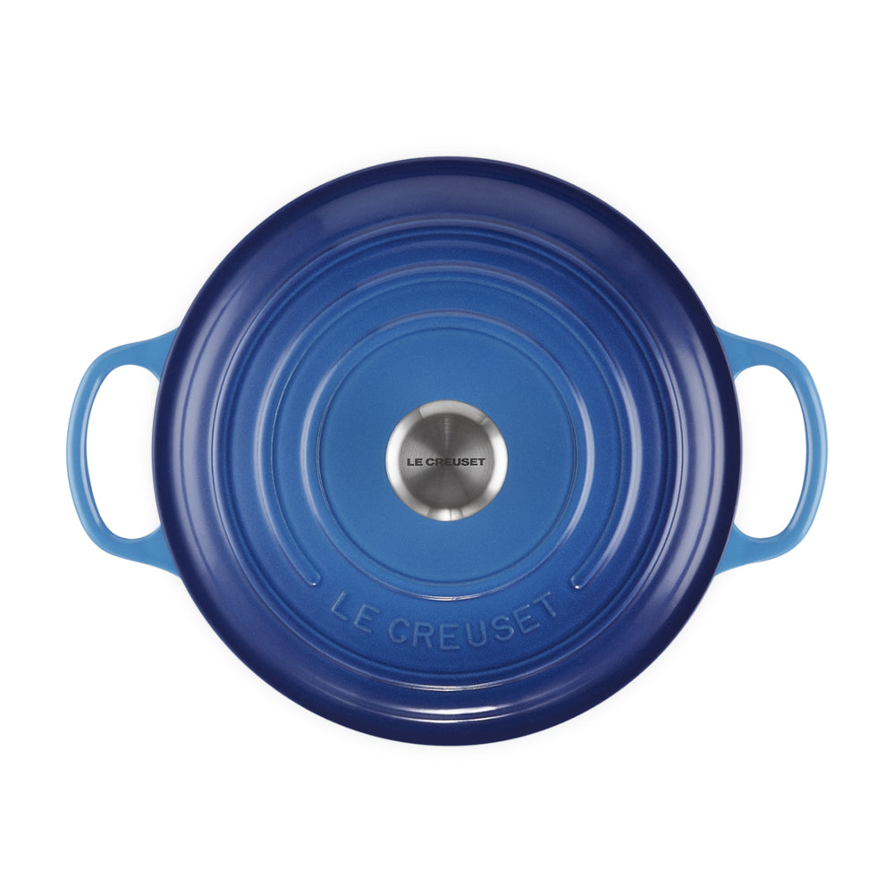 coperchio circolare in ghisa smaltata blu sfumato con manici laterali, centrale in acciaio con scritta Le Creuset, su sfondo bianco