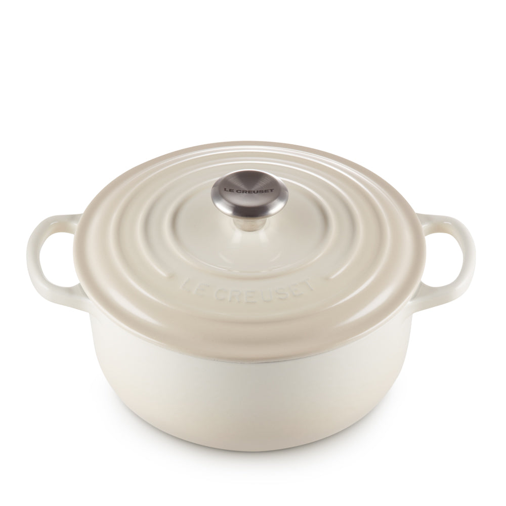 Cocotte rotonda beige in ghisa smaltata con due manici e coperchio con pomello metallico, scritta Le Creuset in rilievo e in nero.