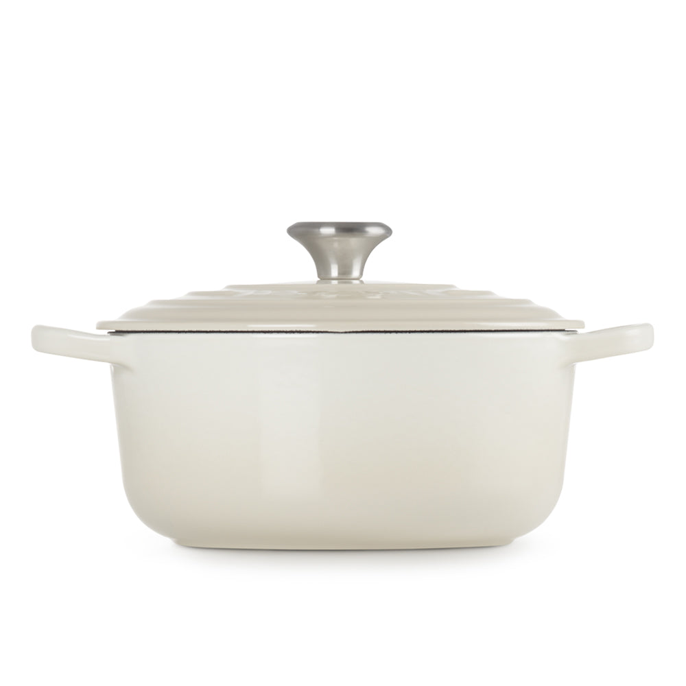 Casseruola smaltata color crema con due manici laterali, coperchio con maniglia metallica e superficie leggermente ondulata, sfondo bianco.