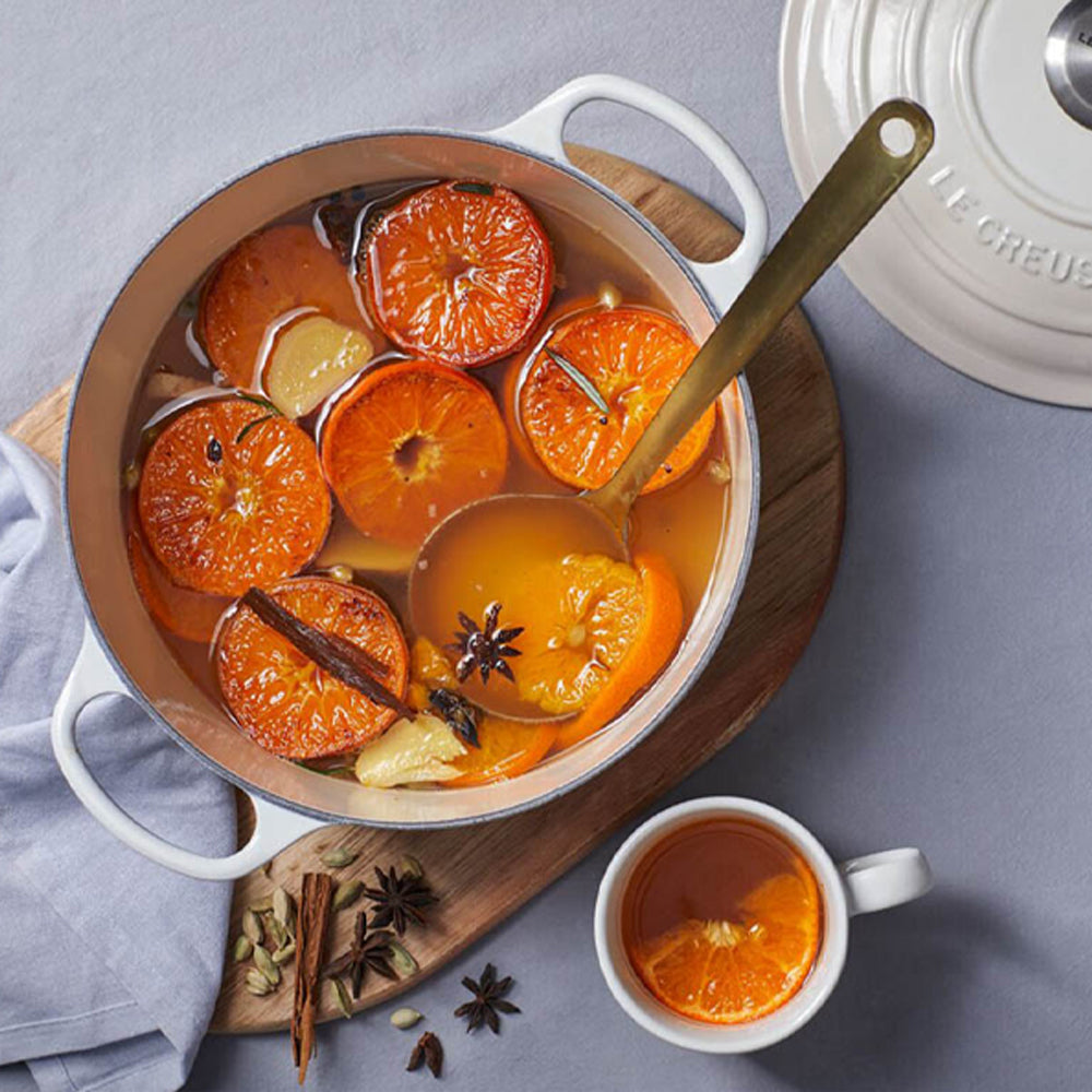 Pentola bianca smaltata con stoviglia arancione, fette di arancia, cannella, anice stellato, zenzero in infuso, accanto tazza bianca con infuso e
