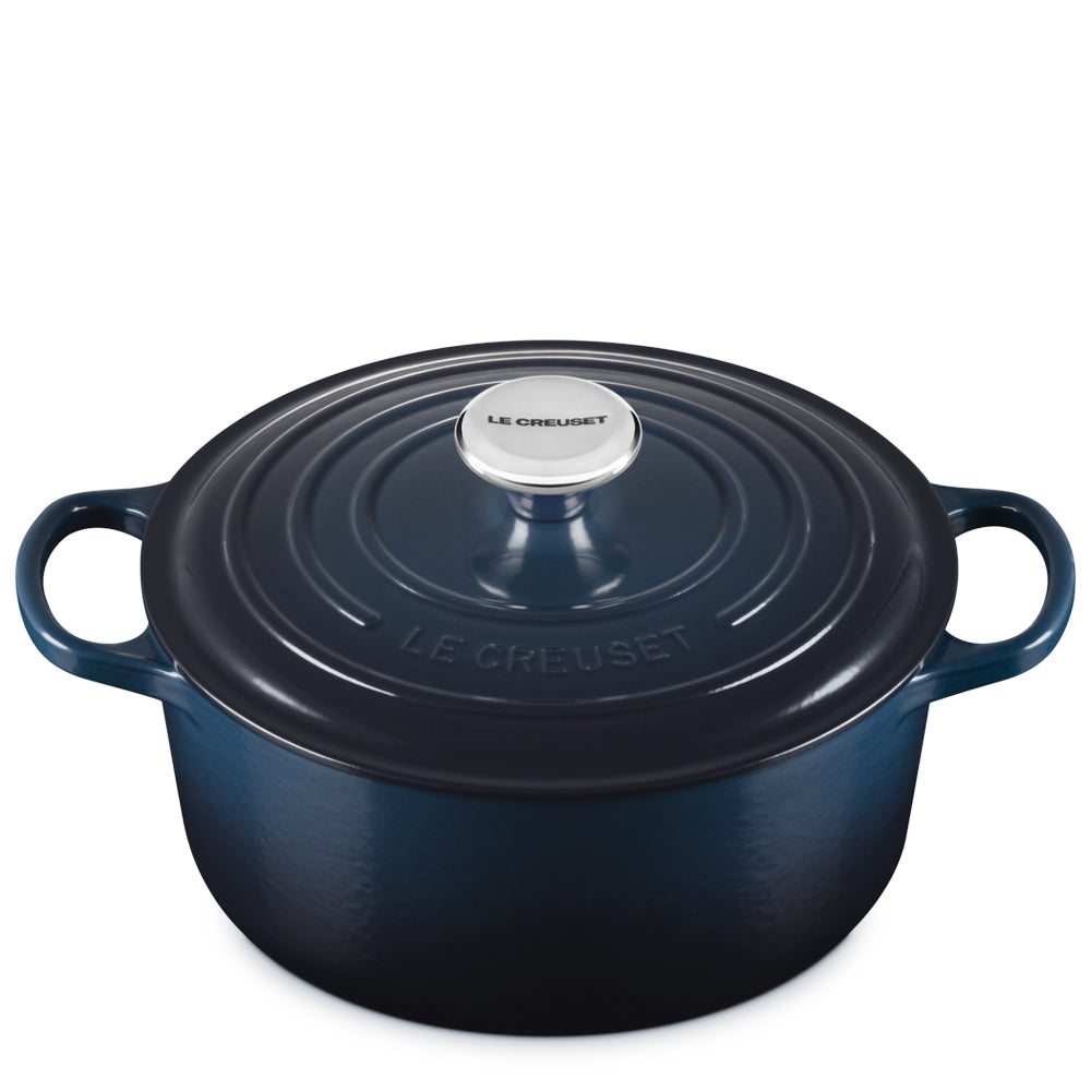 Pentola ovale in ghisa smaltata blu scuro con coperchio e manici integrati, pomello in acciaio con scritta Le Creuset, sfondo bianco.