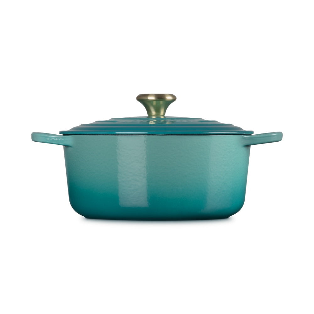 Zeegroene braadpan met handgreep en gouden deksel, schijnbaar geëmailleerd materiaal, op witte achtergrond.