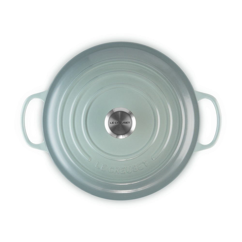 Lichtgroene keramische ronde pan met verlaagde randen en handvatten, merk LE CREUSET, glanzende afwerking en glad oppervlak.