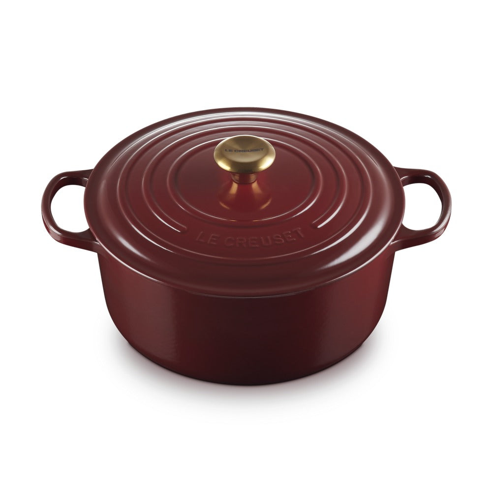 Ronde braadpan van geëmailleerd gietijzer in rood met deksel en gouden handgreep, elementi in relief sulla oppervlak.