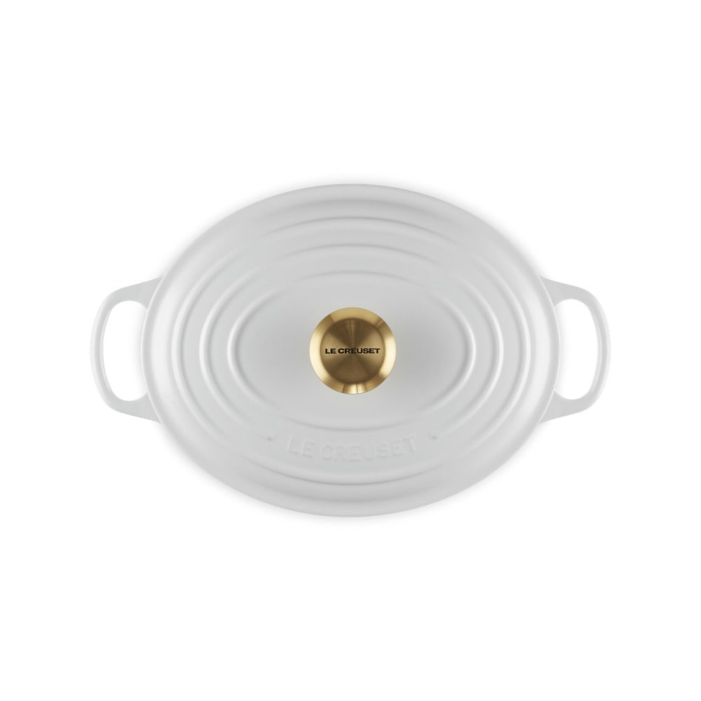 Casserole ovale blanche avec anses et bouton dorato al centro, surface lisse avec lievi dettagli.