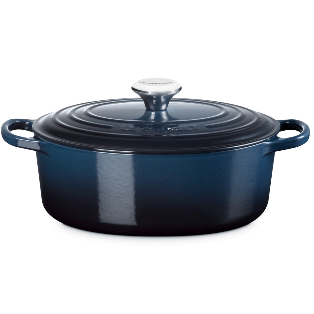 Blauwe ovale geëmailleerde gietijzeren pan met deksel, zijhandgrepen en glanzende metalen knop, neutrale witte achtergrond