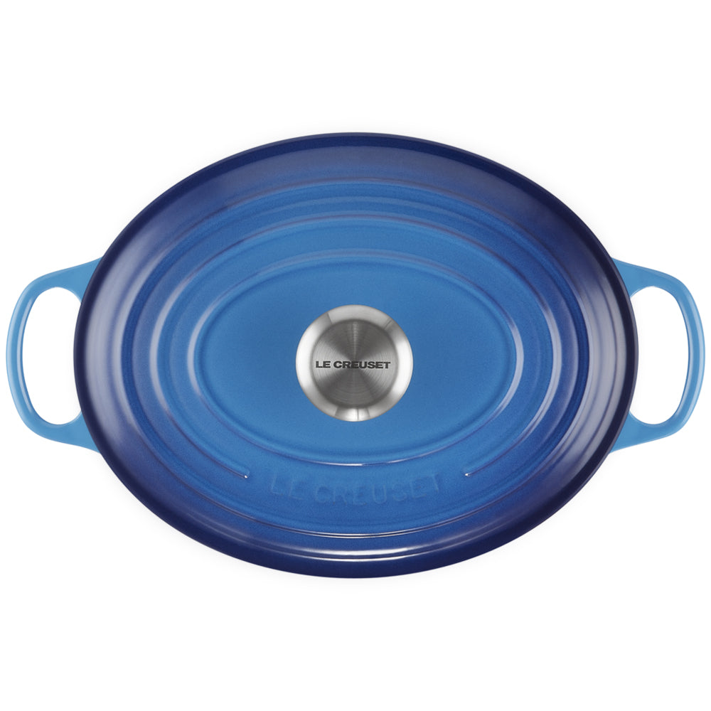 couvercle ovale en fonte émaillée bleu dégradé avec poignées latérales et pomme centrale en métal gravée Le Creuset sur fond blanc
