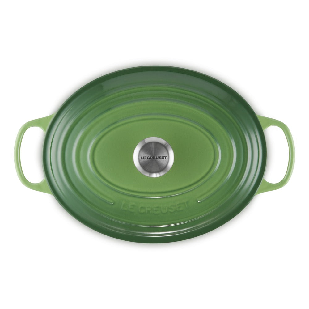 Groene ovale ovenschaal met handvatten, keramiekcoating, met roestvrijstalen bodem met "LE CREUSET"-logo.