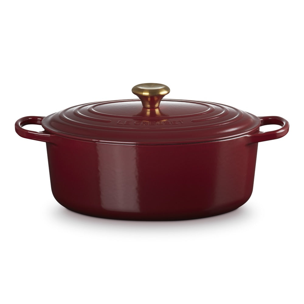 Ronde braadpan van geëmailleerd gietijzer rood, met deksel en gouden handgreep, op witte achtergrond.