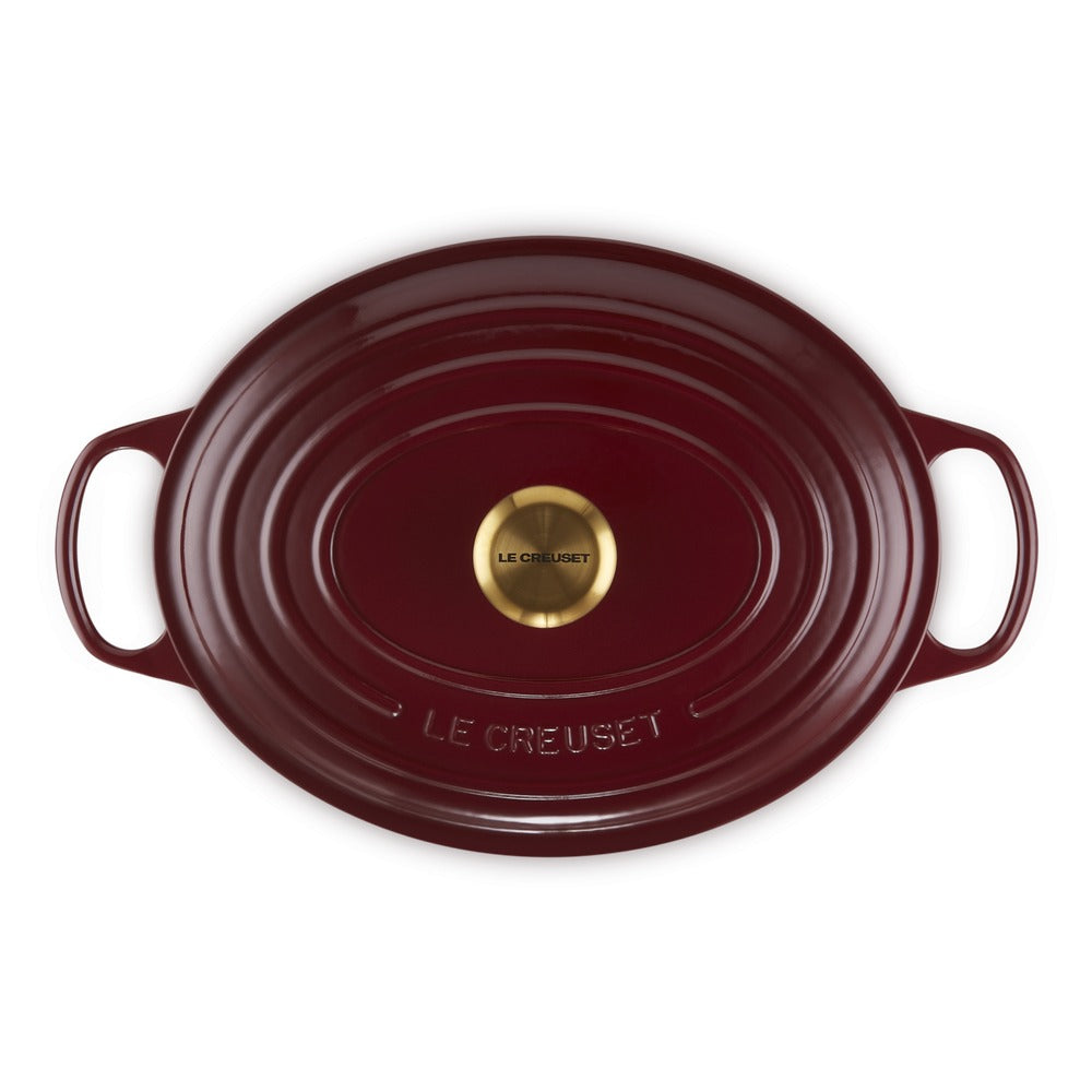 Rode geëmailleerde ovale gietijzeren pan met twee handvatten, gouden bodem en opschrift "LE CREUSET".