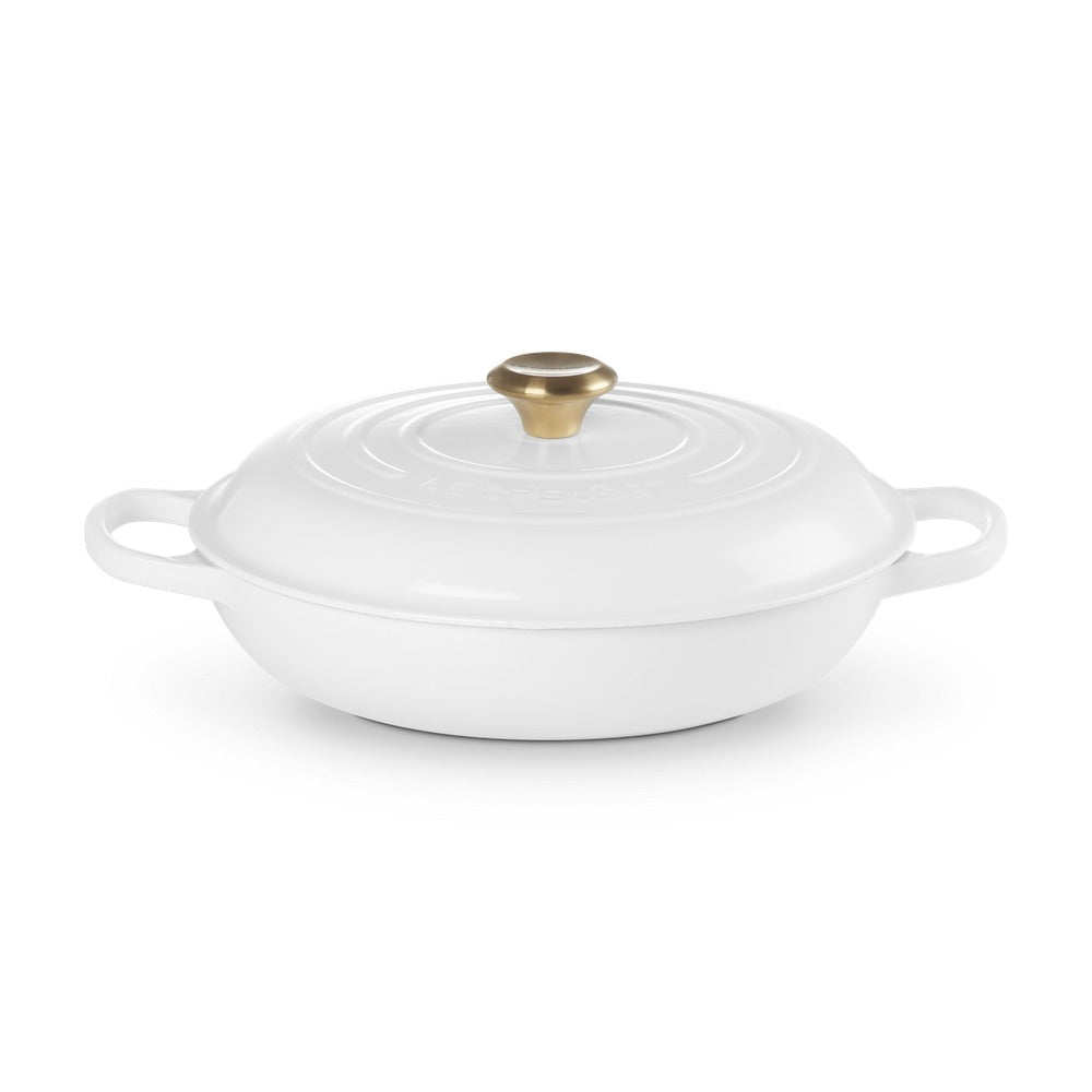Casseruola bianca in ceramica con manico dorato, forma rotonda e bordo inclinato, su sfondo bianco.
