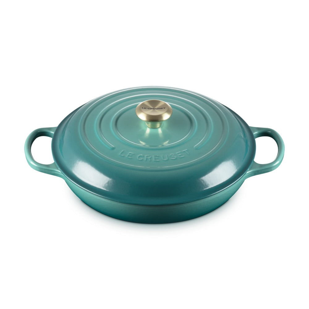 Casseruola ovale in ceramica smaltata verde acqua, con coperchio e manico dorato, superficie liscia e lucida.