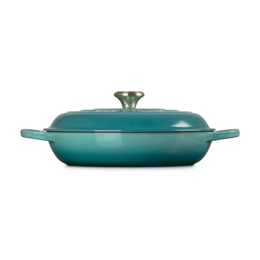 Casseruola rettangolare di colore turchese con coperchio, manico e pomello dorati. Superficie lucida e riflettente.