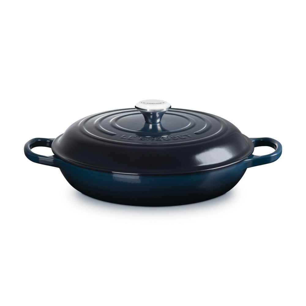Casseruola ovalata in ghisa smaltata, colore blu scuro, con coperchio e manici laterali. Logo "LE CREUSET" visibile.