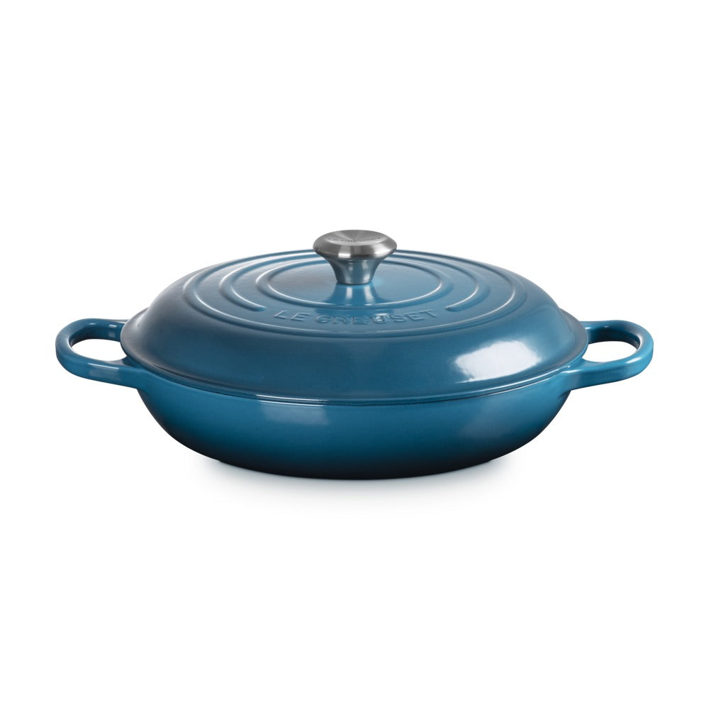 Casseruola ovale in ghisa smaltata blu con coperchio e manico in acciaio inox, superficie liscia e riflettente.