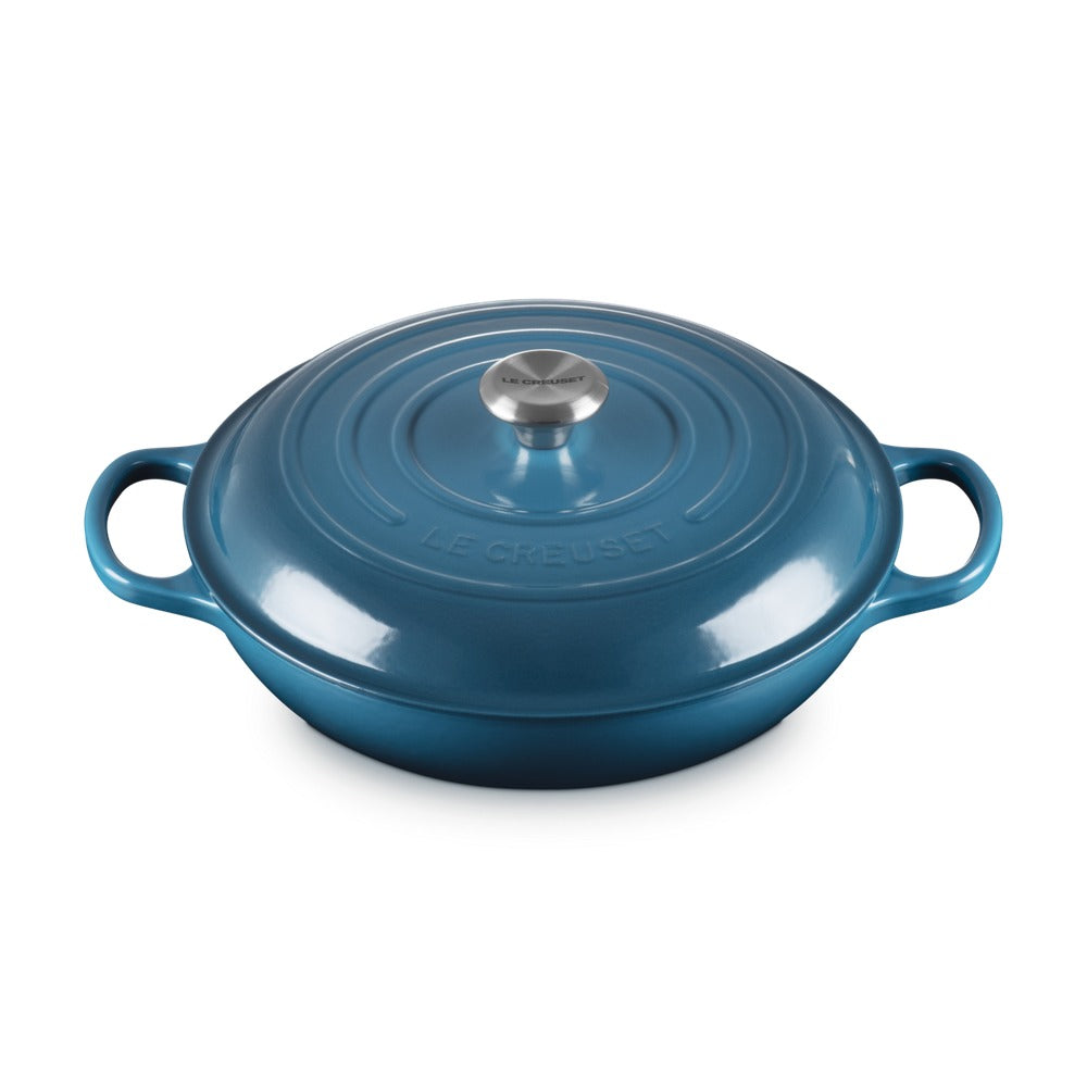 Casseruola ovale smaltata di blu con coperchio e manici laterali, finitura lucida e logo "LE CREUSET" sul corpo.