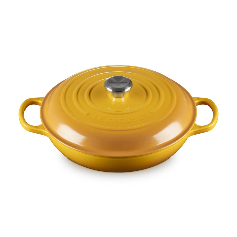 Casseruola rotonda gialla con coperchio, manici laterali, superficie lucida e logo "LE CREUSET" sulla cima.