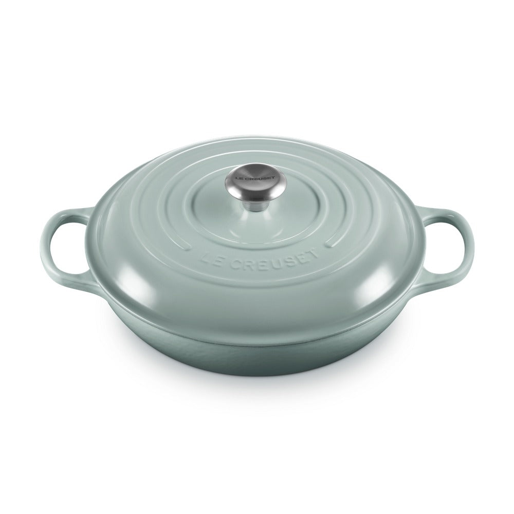 Casseruola ovale verde acqua con coperchio in metallo e manici, superficie lucida, con il logo "LE CREUSET" ben visibile.