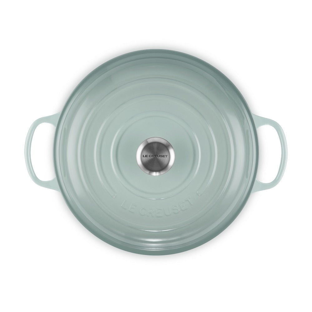 Coperchio di pentola in ceramica verde chiaro con maniglie, superficie liscia e logo in acciaio centrale.