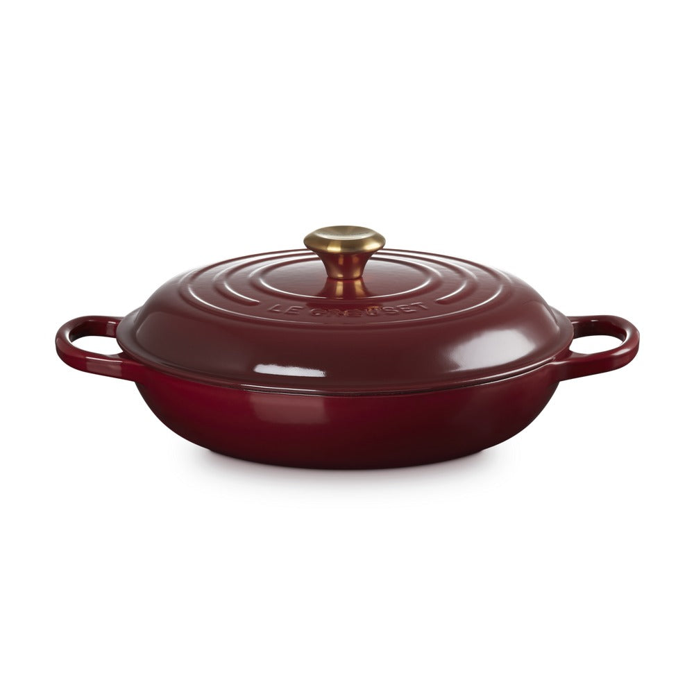 Casseruola rotonda in ghisa smaltata rossa con coperchio e manico dorato, posizionata su sfondo bianco.